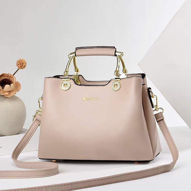 Blush pink structured satchel handbag with gold hardware, top handle, and crossbody strap made of vegan leather for women.